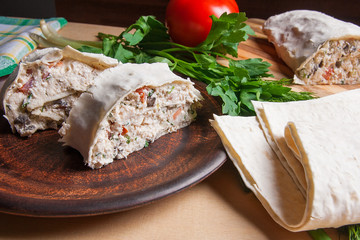 Two pieces of pita bread or lavash roll with cottage cheese or curd, chicken, tomatoes and herbs - dill, onion, parsley on brown clay plate..