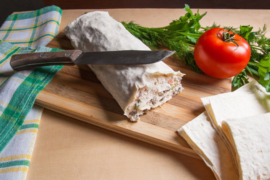 Pita bread or lavash wrapped with cottage cheese or curd, chicken, tomatoes and herbs - dill, onion, parsley. Lavash roll with vintage knife on cutting board.