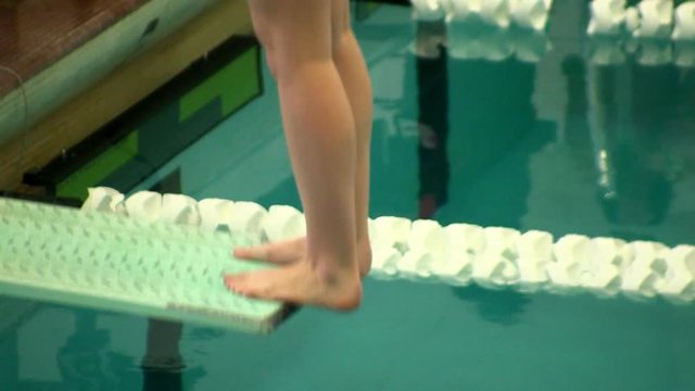 Female diver stands at edge of diving board getting ready to compete in high school meet