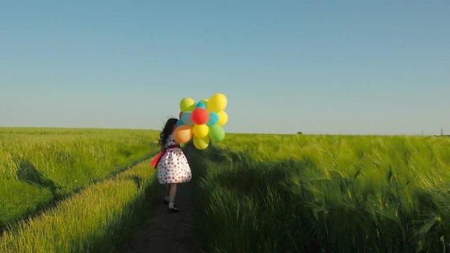 The girl is spinning with balloons on a country road. Beautiful little girl with balloons on the wheat field.