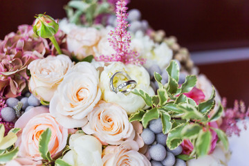 Golden wedding rings with diamonds lie inside rose flower in the bridal bouquet. Symbol of love and marriage.