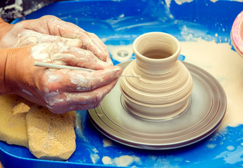 Closeup hands of potter - ceramist master, creating a pattern on a jar at outdoors pottery workshop