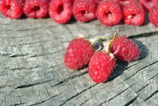 Fresh red natural raspberries branch and rows behind on old cracked wooden background, closeup