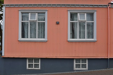 Fototapeta na wymiar Typical Icelandic house facade in salmon pink color made of corrugated iron and with white wooden windows in Reykjavik (the capital city of Iceland) 