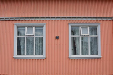 Fototapeta na wymiar Typical Icelandic house facade in salmon pink color made of corrugated iron and with white wooden windows in Reykjavik (the capital city of Iceland) 