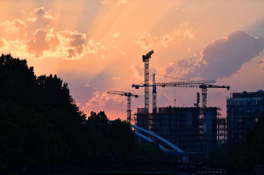 Construction cranes silhouetted against sunset sky