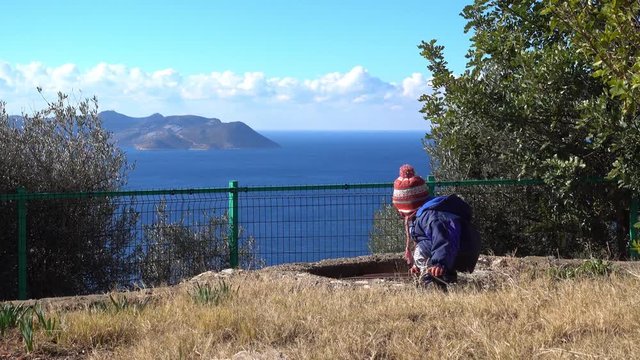 4K Child mischief maker opens a hole, beautiful sea view in the background