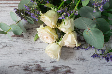 The wonderful white roses with branches of eucalyptus and blue decoration flowers on gray background.