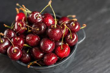 Fresh sweet cherries with water drops in bowl on dark rock table.