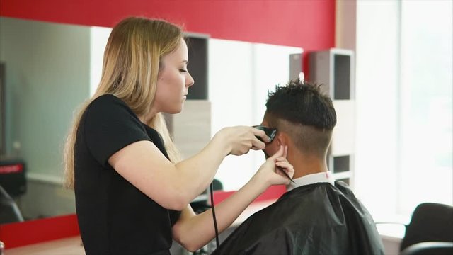A young and professional hair stylist who works in a hair salon shaves the back of the head of the client who came to change the image.