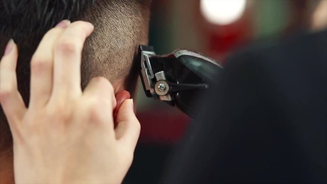Close up shot of the barber's hands, who cuts the hair of the man on his head, the hair stylist uses an electric hair machine to change the length of the hair behind