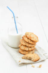 .A stack of cookies and a bottle of milk with a straw on a light wooden table against a white background.