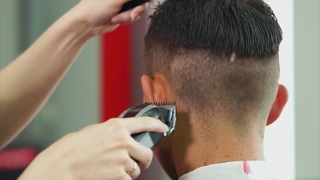 The modern stylist cuts her hair with a shaving machine and scissors, the woman neatly changes the length of the hair of a visitor to the barbershop