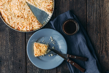 Pie entirely and a piece of cake on a blue plate with fork and knife, cup of coffee on old wooden table, top view. Breakfast.