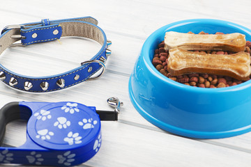 From above blue leather strap, bones on bowl of puppy chow on wooden table.