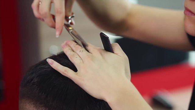Woman hairdresser making haircut to young man. She using scissors and comb. Close up view