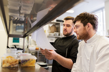 chef and cook with lists or bills at kitchen