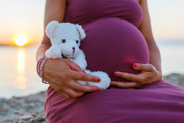 Donna in gravidanza al mare si si accarezza la pancia con peluche per bambino