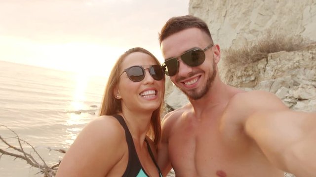 Happy couple taking selfie on beach at sunset using phone smiling and spinning enjoying nature and lifestyle on vacation