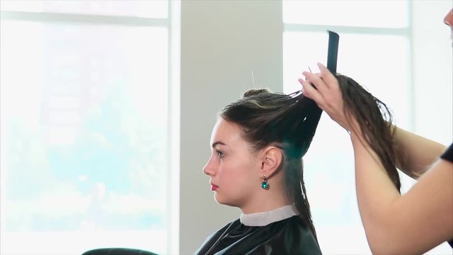 A hair stylist with her hair down pins wet hair in order to dry them with a hair dryer, the client of the beauty salon is waiting for the hairstyle to finish
