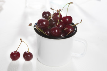 the Uzbek ripe cherry in an enameled cup on a white wooden table. Copy space