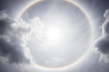 Sun with circular rainbow sun halo with gray clouds at noon.