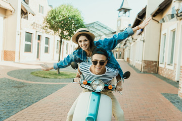 Happy stylish young couple riding scooter  and smiling at camera