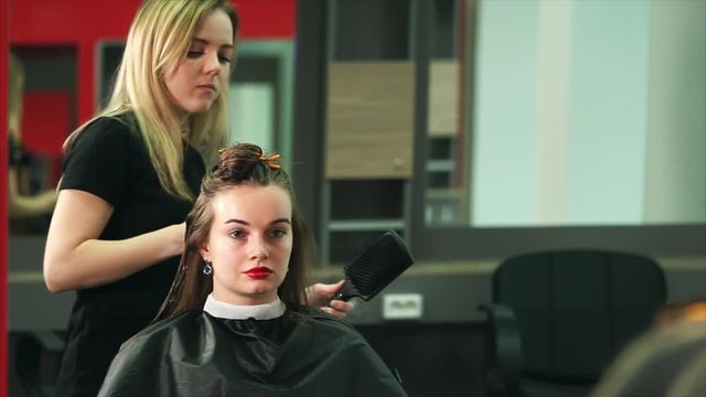 A young and professional hair stylist dries the client's long hair with a hairdryer, a hairdresser helps himself with a comb, a beauty salon expects a beautiful hairstyle