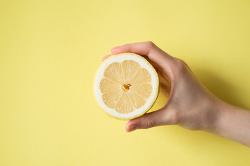 Lemon in woman's hand on a yellow background