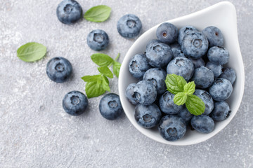 Fresh organic blueberries in white bowl. Juicy berries and mint leaves on a stone or concrete background. Natural antioxidant superfood. healthy food concept