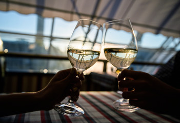 Friends clinking wine glasses above dinner table. Young couple drinking white wine in a cozy 5star Italian restaurant.