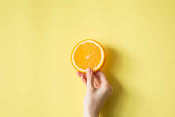 Hand holding orange on yellow background food concept