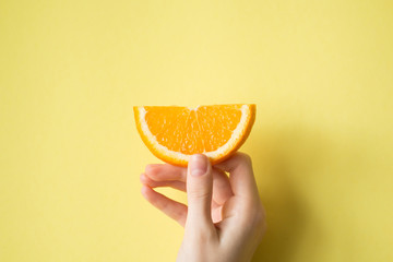 Hand holding orange on yellow background food concept