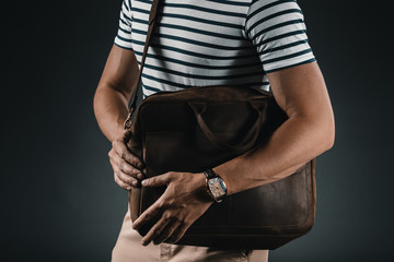 cropped view of stylish man in striped t-shirt holding leather bag, isolated on grey