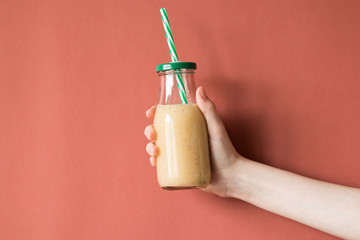 Woman hand holding smoothie shake against colored wall. Drinking yellow healthy smoothie concept.