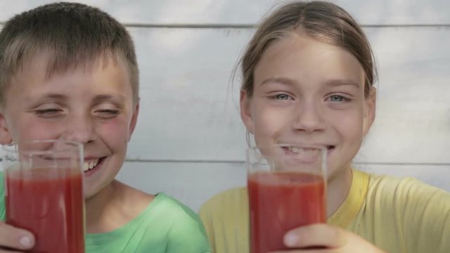 Children on a white background drink tomato juice from glasses. Two boys drink tomato juice.

