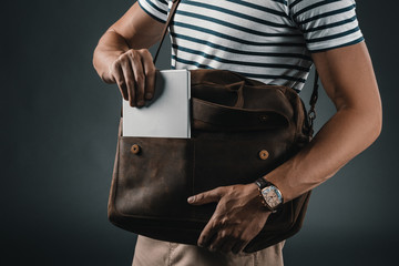 Cropped shot of stylish man putting digital tablet into brown leather shoulder bag