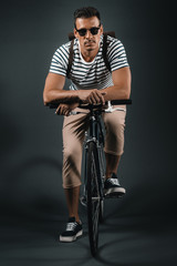 Fototapeta na wymiar serious man in sunglasses looking at camera while sitting on bicycle isolated on grey