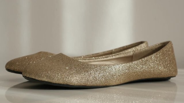 Pair of golden colour ballet flats on white close-up slow tilt 4K 2160p 30fps UltraHD footage - Elegant evening shoes 3840X2160 UHD tilting video 