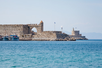 Harbor and monuments in Rhodes. Old defensive stands and windmills. Wharf harbors, boats and sailing ships. Historic harbor, pier and beach.