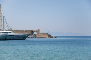 Harbor and monuments in Rhodes. Old defensive stands and windmills. Wharf harbors, boats and sailing ships. Historic harbor, pier and beach.