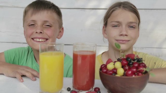 Boys drink orange and tomato juice. Children drink juice looking in a movie camera.
