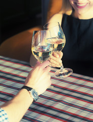 Friends clinking wine glasses above dinner table. Young couple drinking white wine in a cozy Italian restaurant.