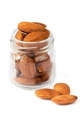 Three apricot kernels nearby small glass jar isolated on white background