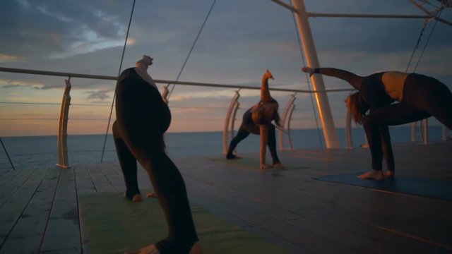 Silhouette group women trikonasana asanas yoga class sea dawn slow motion