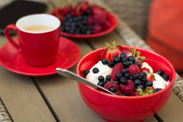 Healthy breakfast on garden furniture: cottage cheese with sour cream, strawberry, raspberry and blueberry, espresso and plate of fresh ripe berries on wooden garden furniture. Selective focus