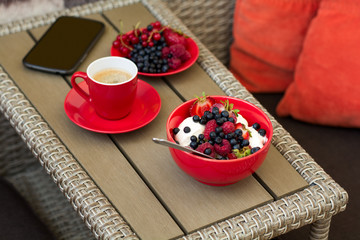 Healthy breakfast on garden furniture: cottage cheese with sour cream, strawberry, raspberry and blueberry, espresso and plate of fresh ripe berries on wooden garden furniture. Selective focus