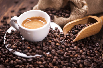 Zbliżenie filiżanki kawy nad ciemnymi palonymi ziarnami kawy