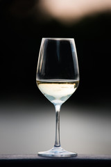 A glass of the white wine standing on the wooden surface.