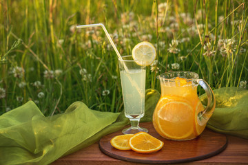 Two glass jars with lemonade on a wooden stand on the grass. Soda in a jar with a lid. Breakfast on the grass.